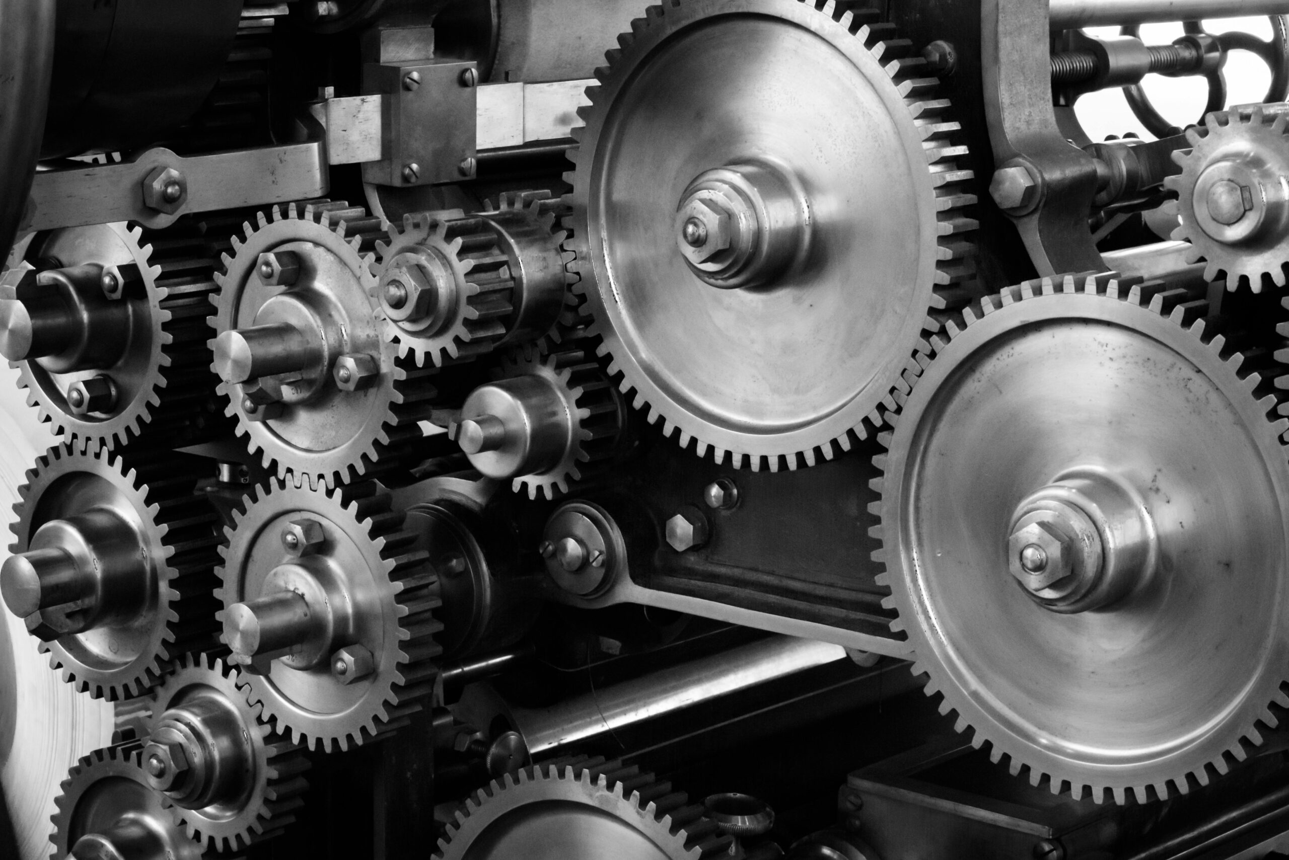 Services Close-up view of a complex industrial gear mechanism in black and white.
